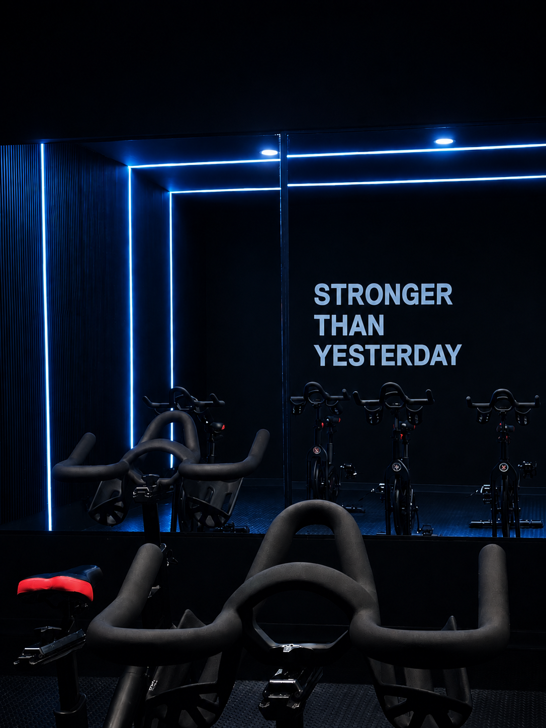 Row of spin bikes in front of a mirrored wall with 'Stronger than yesterday' signage and blue neon lighting